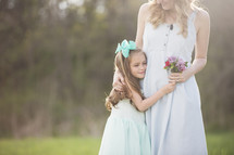 mother and daughter hugging with flowers outdoors 