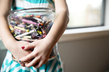 a girl child holding a jar of crayons 