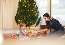 a girl opening a gift by a Christmas tree