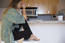 a woman in her pajamas praying in the kitchen