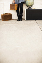 woman holding luggage and standing next to a globe 