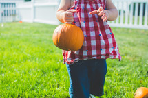 a toddler carrying a small pumpkin 