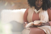 a woman sitting on a couch reading a Bible.