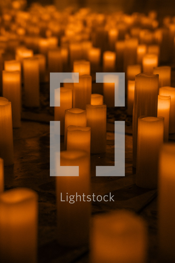 Lots of candles on a church floor, candle light glowing orange