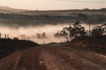 fog rising over a dirt road and village view 