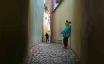 toddler girl holding a doll standing in an alley 