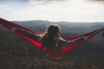 a young woman relaxing in a hammock on a mountaintop 