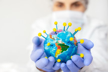 Coronavirus pandemic in world, woman scientist holding in her hand the earth globe that is shaped like a coronavirus