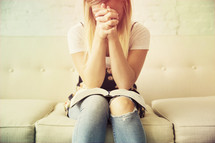 woman sitting on a couch in prayer with an open Bible in her lap.