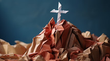 Origami cross on a hill made of crumbled paper. 