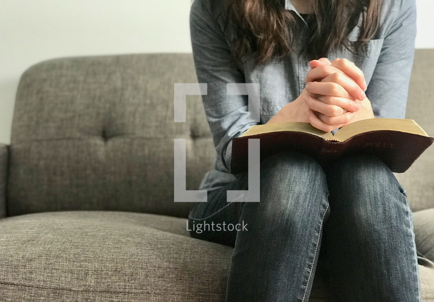 A woman sitting on a sofa praying with her Bible