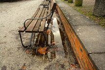 puddle and fall leaves under a park bench 