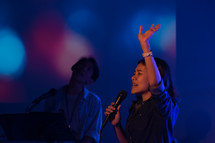 woman singing into a microphone with hand raised 