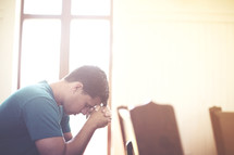 Man with clasped hands and bowed head praying in a church pew.