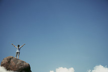 woman standing on top of a rock with her hands raised in worship 