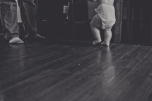 A baby walking toward its father.