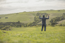 a man standing with raised arms in a field of green grass 