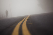 man riding a bike on a road under thick fog