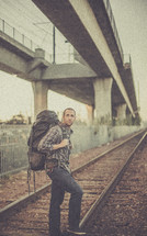 man standing on railroad tracks with a backpack 