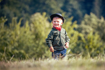 Cute Little Happy Boy with Hat and Bandana in Green Summer Forest