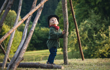 Little Cute Blond Boy in a Hat in Nature between Wooden Logs