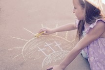 A little girl drawing three Easter crosses with sidewalk chalk 