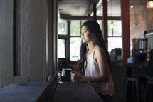 a young woman listening to earbuds in front of a window in a coffee shop.