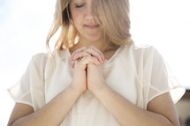 a woman with praying hands outdoors 