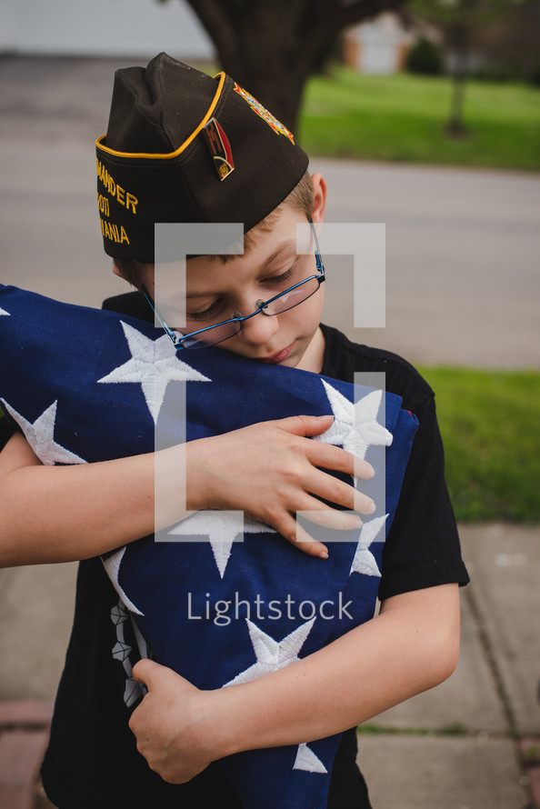 child carrying a folded flag and wearing a military cap 
