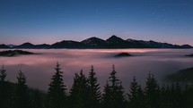 Panoramic view of foggy forest in mountains nature landscape with blue starry night sky with fast motion stars Time lapse
