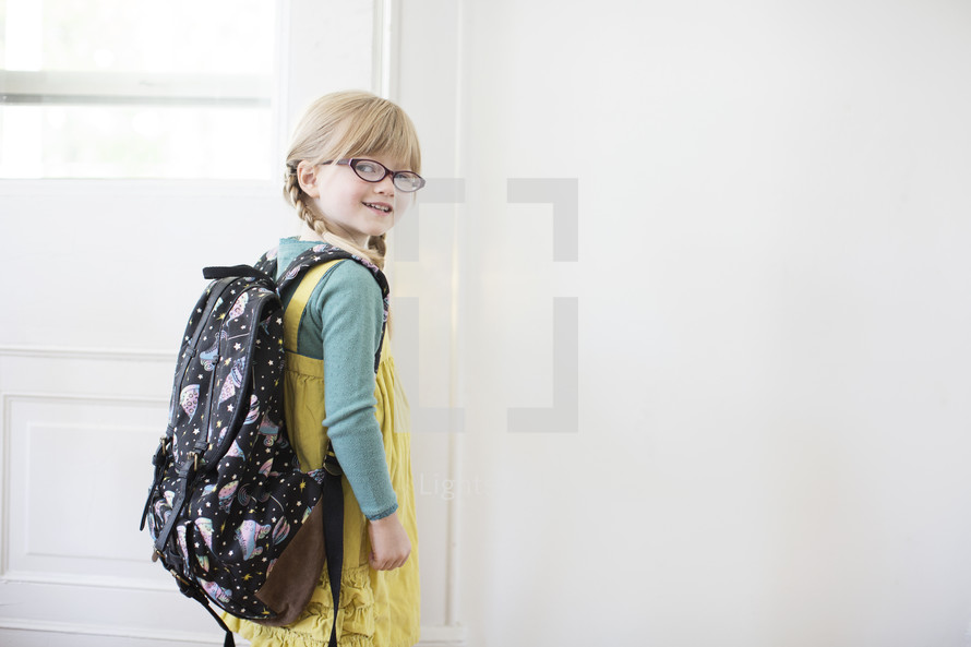 girl child with a book bag opening a door 