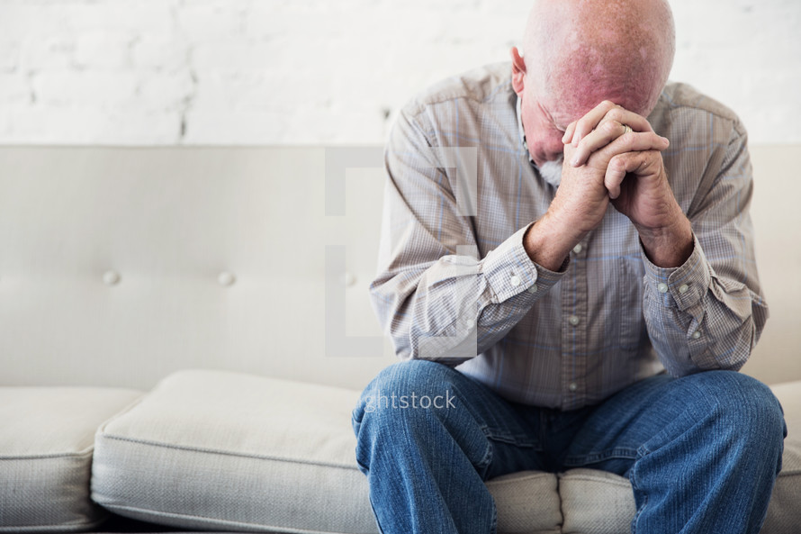 a man sitting on a couch with head bowed in prayer 