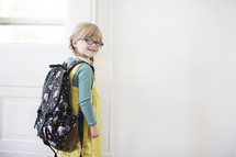 girl child with a book bag opening a door 