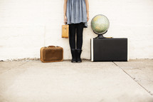 Girl holding a suitcase and standing next to a globe 