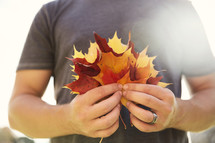 a man holding a handful of fall leaves 