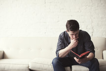Man sitting on a sofa reading the Bible.
