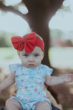 an infant girl in a red headband and bow