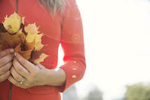a woman holding a handful of fall leaves 