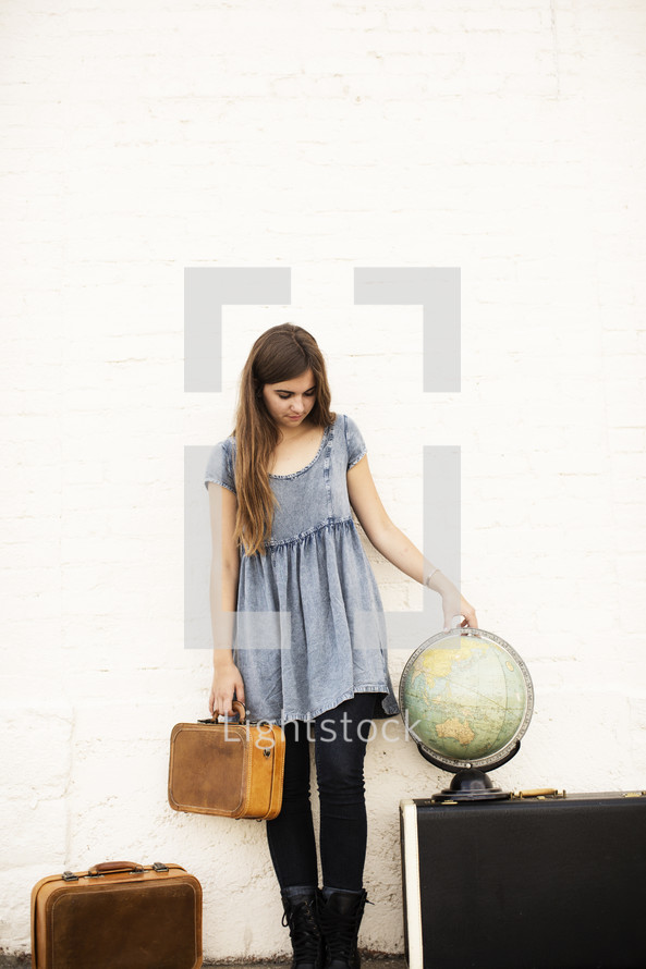 woman holding luggage standing next to a globe