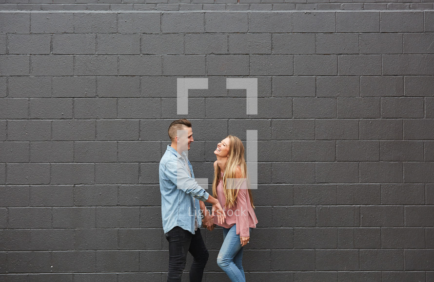 a couple standing in front of a gray brick wall 