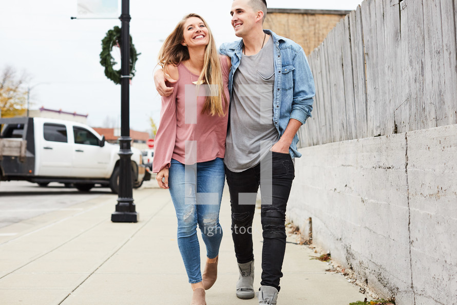 a couple walking down a sidewalk with arms around each other 