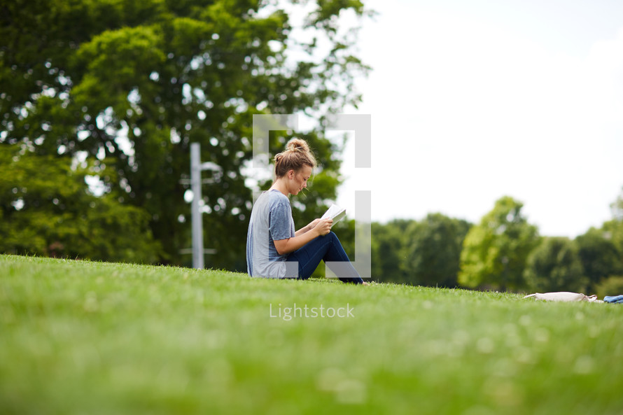 a person sitting in the grass reading a Bible 