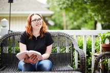 a young woman sitting on a porch reading a Bible 
