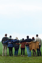 a united group of people standing with arms around each other 