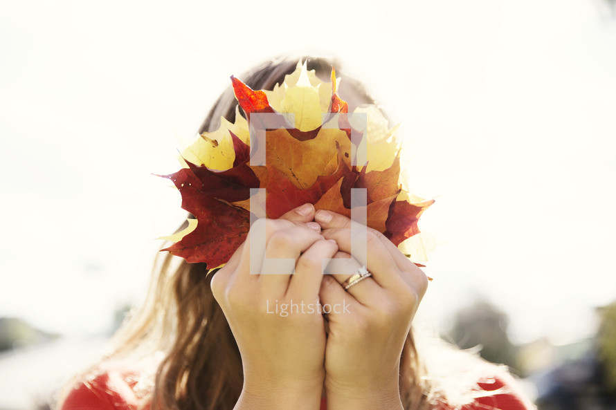 a woman holding fall leaves in front of her face