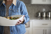 a woman holding a large bowl of salad 