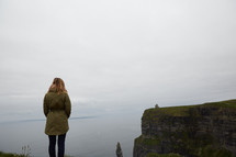 a woman standing at the edge of a cliff looking out at the ocean 