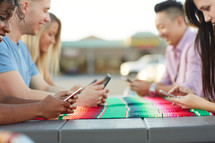 friends sitting together at an outdoor table texting
