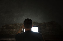 man looking at a computer screen in darkness.
