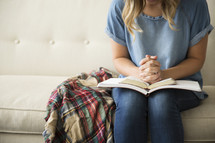 a woman sitting on a couch reading a Bible and praying 